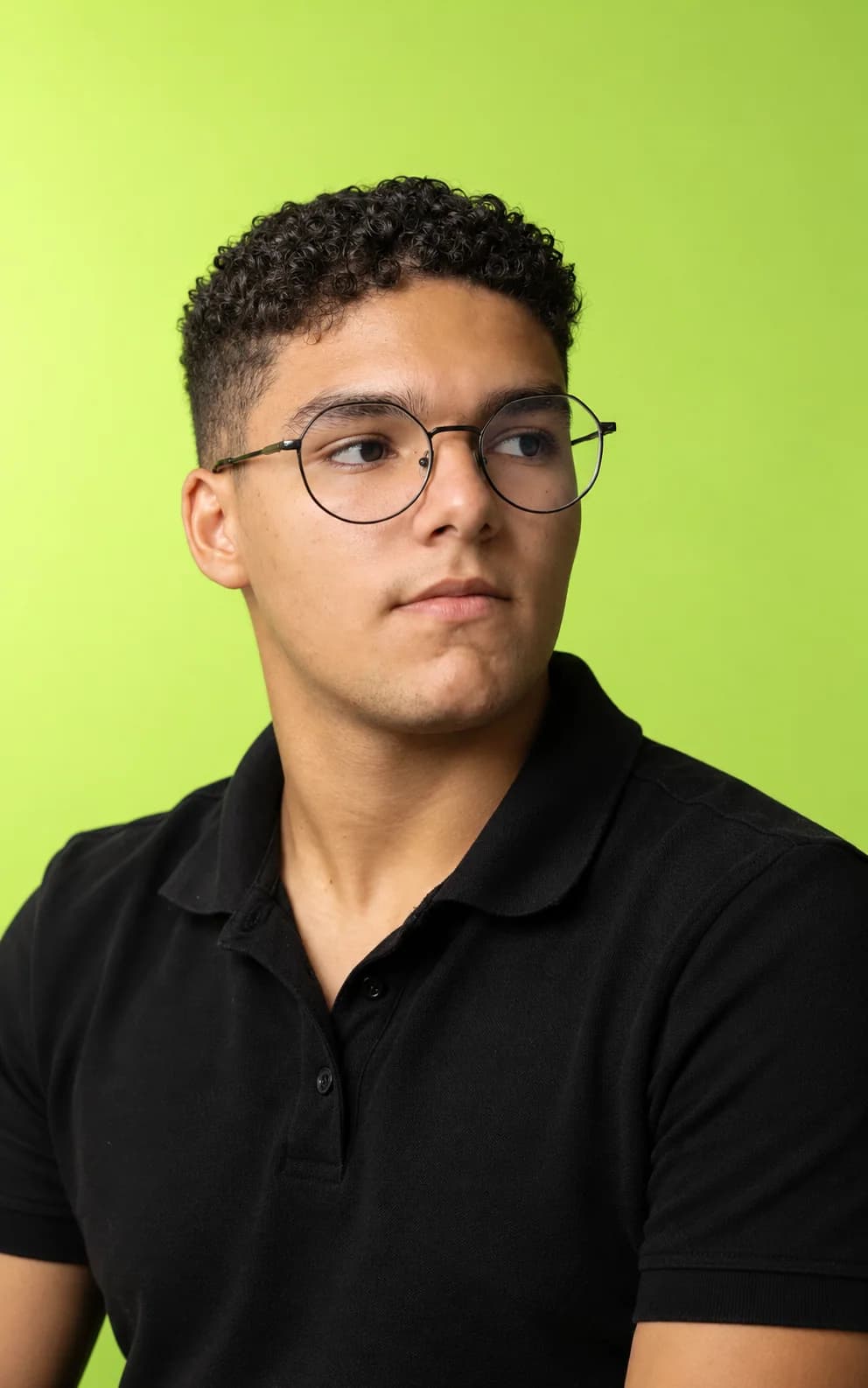 Anthony Gabriell, de óculos e camisa polo preta, olhando para o lado sobre fundo verde-lima